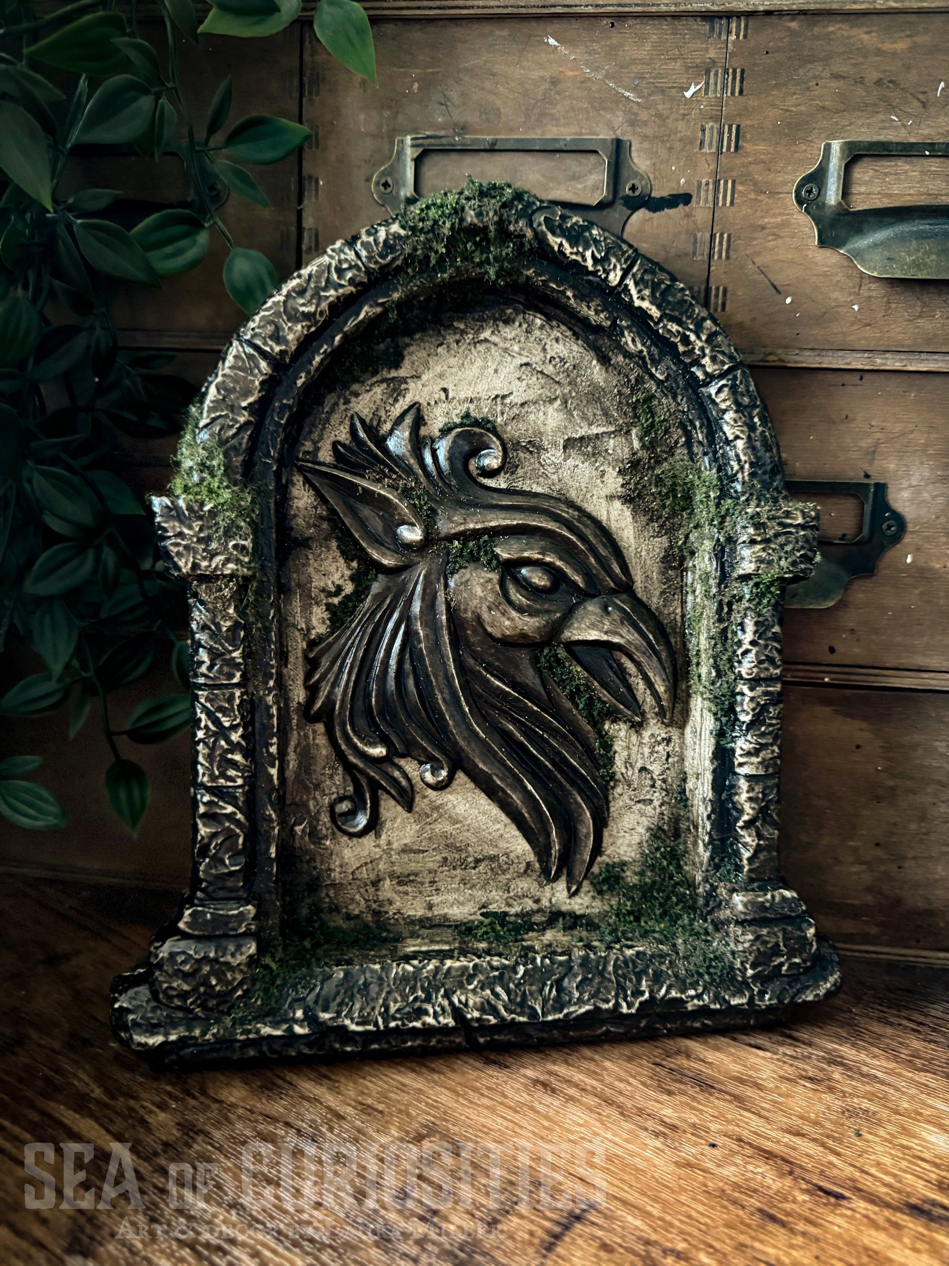 Decorative sculpted stone wall arched window with Griffin head, branded 'Sea of Curiosities'.